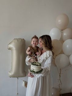 a woman holding a baby while standing next to a cake