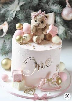 a teddy bear sitting on top of a pink and white cake with gold decorations around it