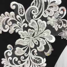 the back of a black dress with white lace on it and an embroidered flower design