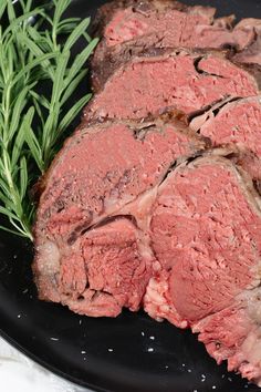 some meat is on a black plate with green sprigs next to the meat