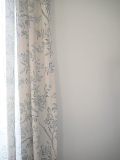 a cat sitting on top of a window sill next to a curtain with flowers