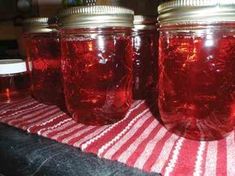 four jars are lined up on a red and white table cloth, one is empty