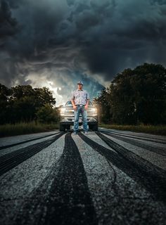 a man standing in the middle of a road next to a car and storm clouds