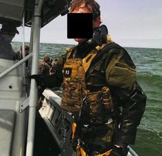 a man standing on the back of a boat in the middle of the ocean, wearing a diving suit and goggles