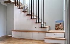 an empty room with white cabinets and wooden stairs in front of a painting on the wall