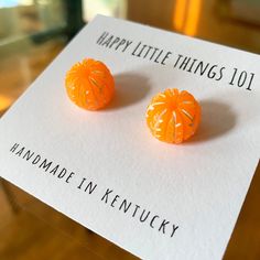 an orange pair of earrings sitting on top of a piece of paper that says happy little things 101