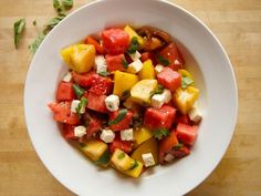 a white bowl filled with watermelon, pineapple and feta cheese