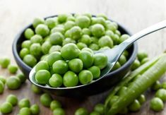 a spoon full of green peas sitting on top of a wooden table