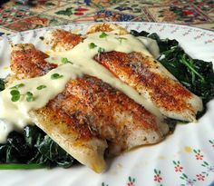 a plate topped with chicken covered in sauce and greens on top of a floral table cloth