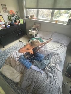 a person sitting on top of a bed with an electric guitar in their hand and looking out the window