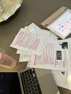 an open laptop computer sitting on top of a desk next to papers and a cup