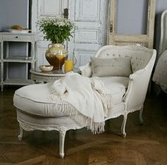 a white chaise lounge chair sitting on top of a hard wood floor next to a bed