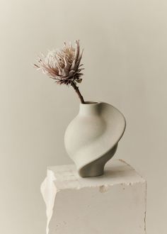 a white vase with a flower sticking out of it's top on a block