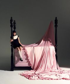 a woman sitting on top of a bed covered in pink sheets and draping