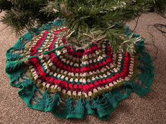 a crocheted christmas tree skirt on the floor next to a pine tree branch