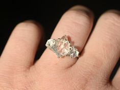 a person's hand holding an engagement ring with three diamonds on it and the middle finger