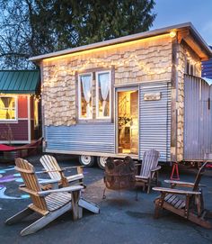 the tiny house is lit up with fairy lights and sits in front of two adiron chairs