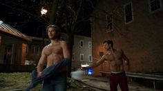 two shirtless men standing next to each other in front of a building at night