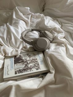 an open book and headphones on top of a white sheeted bedspread