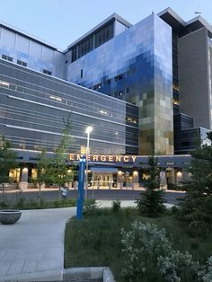 the entrance to an emergency department building at dusk with trees and bushes in front of it