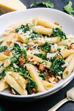 a white bowl filled with pasta and spinach on top of a blue table cloth