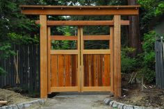 an open wooden gate in the middle of a yard with trees and bushes behind it