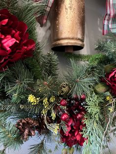 a christmas wreath with pine cones, red berries and greenery next to a golden bell