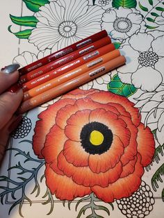 a person holding four pencils in their hand next to a drawing book with flowers on it