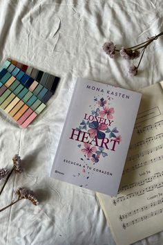 a book sitting on top of a bed next to some flowers and music sheets in front of it