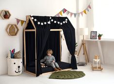 a little boy sitting in a black tent bed next to a green rug on the floor