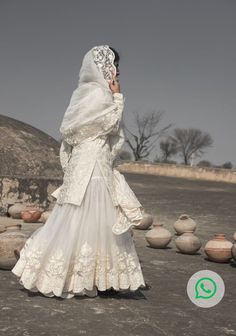 a woman in a white dress and veil is standing near some pottery pots on the ground