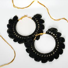 two black crocheted hoop earrings on a white surface with a gold chain attached to it