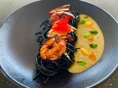 a black plate topped with pasta and shrimp