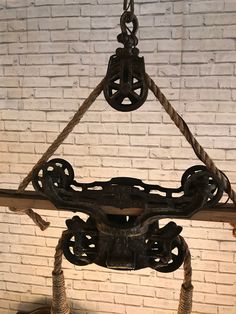 an iron sculpture hanging from a rope in front of a white brick wall and floor