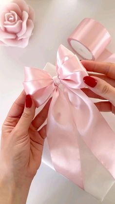 a woman's hands holding a pink ribbon with a rose in the back ground