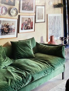 a green couch sitting in front of a wall with pictures hanging on it's side