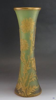 a green and gold vase with flowers on the bottom is sitting in front of a gray background