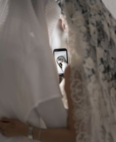 a woman in a white dress is holding a cell phone and looking at the screen