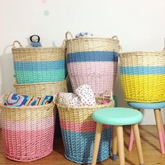 four baskets are stacked on top of each other in different colors and sizes, along with two stools