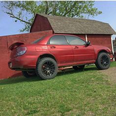 a red car parked in front of a barn