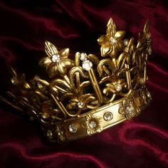 a gold tiara with flowers and leaves on it's side, sitting on a red velvet background