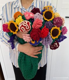 a woman holding a bouquet of crocheted flowers in her hands and wearing a striped shirt