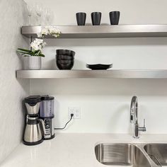 a kitchen with stainless steel sink and shelving above the sink is filled with dishes