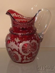 a red and white glass pitcher sitting on top of a counter next to a wall