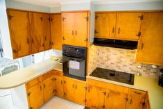 an empty kitchen with wooden cabinets and black stove top oven in the center, surrounded by white counter tops