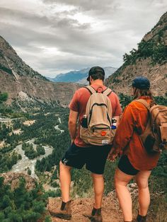 two people standing on top of a mountain looking at the valley below