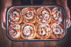 a person holding a pan filled with cinnamon rolls