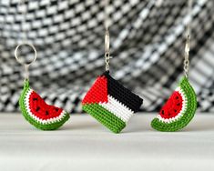 two knitted watermelon slices hanging from hooks on a white surface with black and white checkered background