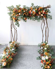 an arch made out of branches with flowers and leaves on it, sitting in front of a wall