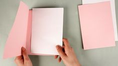 two hands holding pink and white papers next to each other